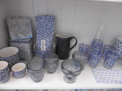 Eine Sammlung blau-weiß gemusterter Küchenutensilien auf einem Regal, darunter Schüsseln, Tassen, Teller, ein Krug und Vasen.
