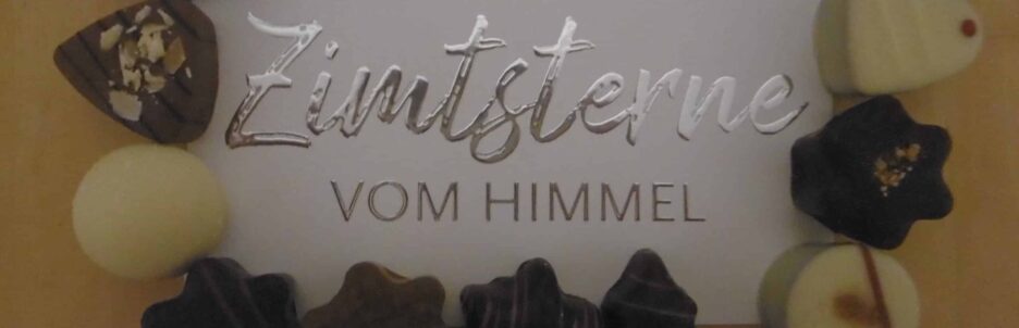 Verschiedene Schokoladenpralinen sind rund um eine Karte mit dem deutschen Text „Ich hole dir die Zimtsterne vom Himmel“ arrangiert, die auf einer Holzoberfläche liegt. {{brizy_dc_image_alt entityId=